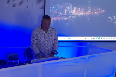 Homme debout devant un ordinateur portable, dans une salle éclairée par des lumières bleues, avec une projection en arrière…