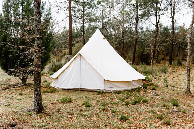 Tente beige en toile installée dans une clairière entourée d'arbres.