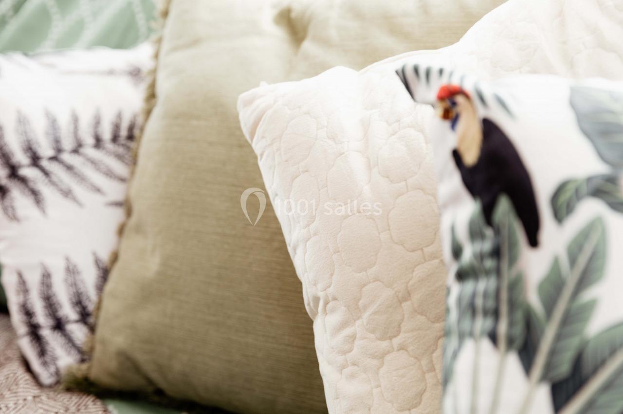 Coussins décoratifs aux motifs végétaux et tropicaux, disposés sur un lit ou un canapé.