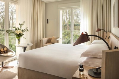 Salon lumineux avec canapé beige, table en bois, suspension noire, bouquet de fleurs et grandes fenêtres.