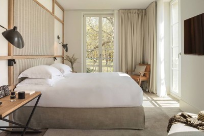 Salon lumineux avec canapé beige, table en bois, suspension noire, bouquet de fleurs et grandes fenêtres.