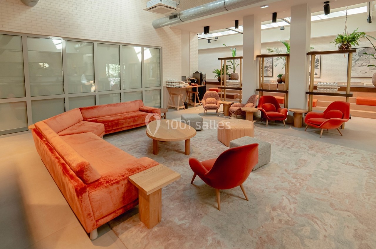 Salon moderne avec canapé et fauteuils rouges, tables en bois clair, plantes et lumière naturelle.