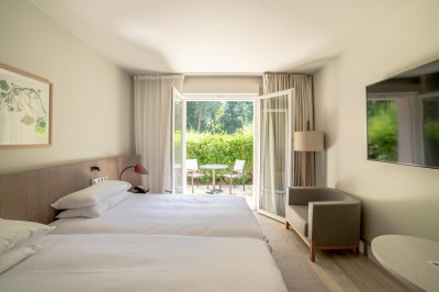 Salon lumineux avec canapé beige, table en bois, suspension noire, bouquet de fleurs et grandes fenêtres.