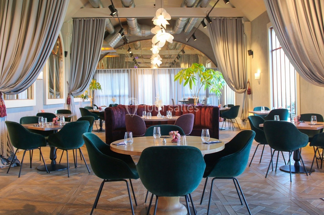 Salle de restaurant élégante avec tables en bois, chaises vertes, rideaux gris et plantes décoratives.