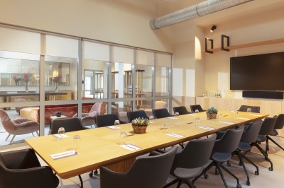 Salon lumineux avec canapé beige, table en bois, suspension noire, bouquet de fleurs et grandes fenêtres.