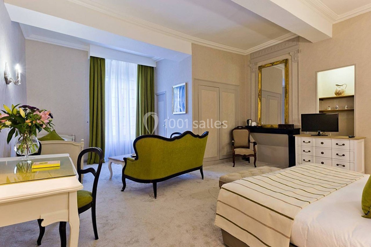 Chambre lumineuse avec lit double, canapé vert, bureau, télévision et grande fenêtre avec rideaux verts.