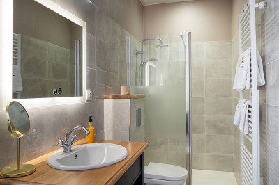 Salle de bain moderne avec douche à l'italienne, lavabo sur plan en bois, miroir éclairé et porte-serviettes mural.
