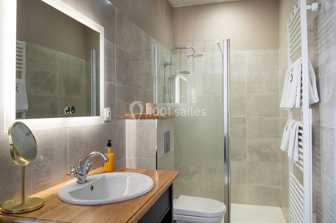 Salle de bain moderne avec douche à l'italienne, lavabo sur plan en bois, miroir éclairé et porte-serviettes mural.
