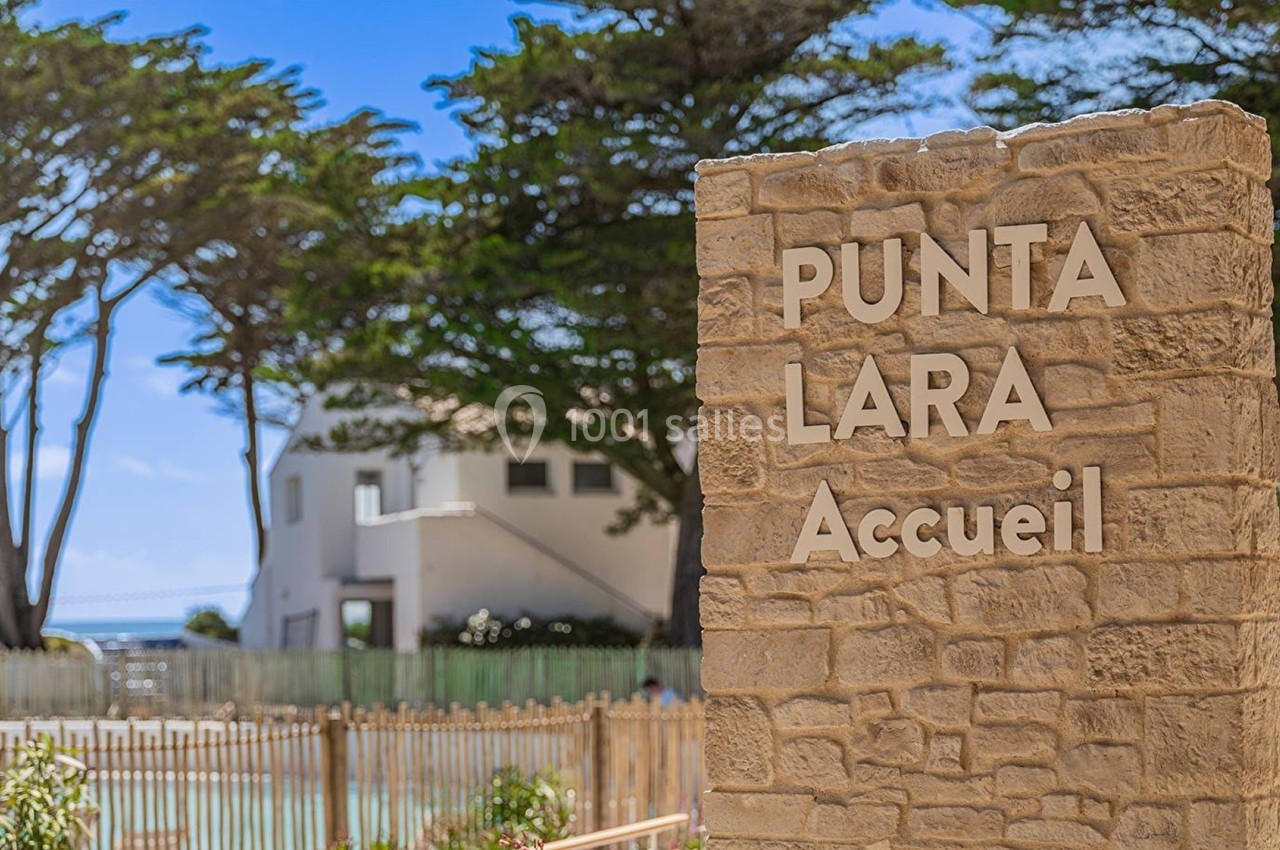 Panneau en pierre indiquant ’Punta Lara Accueil’ devant un bâtiment blanc entouré d'arbres et de végétation.