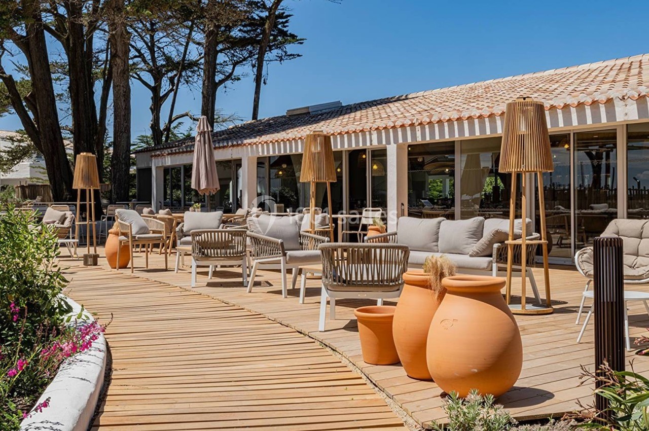 Terrasse en bois avec mobilier d'extérieur, pots en terre cuite et parasols, entourée de végétation et d'arbres.