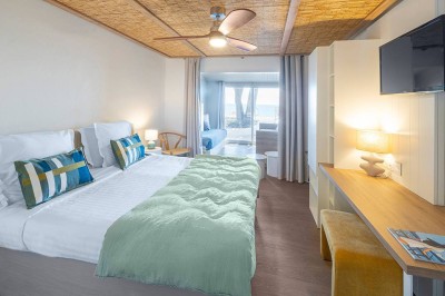 Piscine extérieure entourée de chaises longues et de tables, avec des bâtiments blancs et des arbres en arrière-plan.