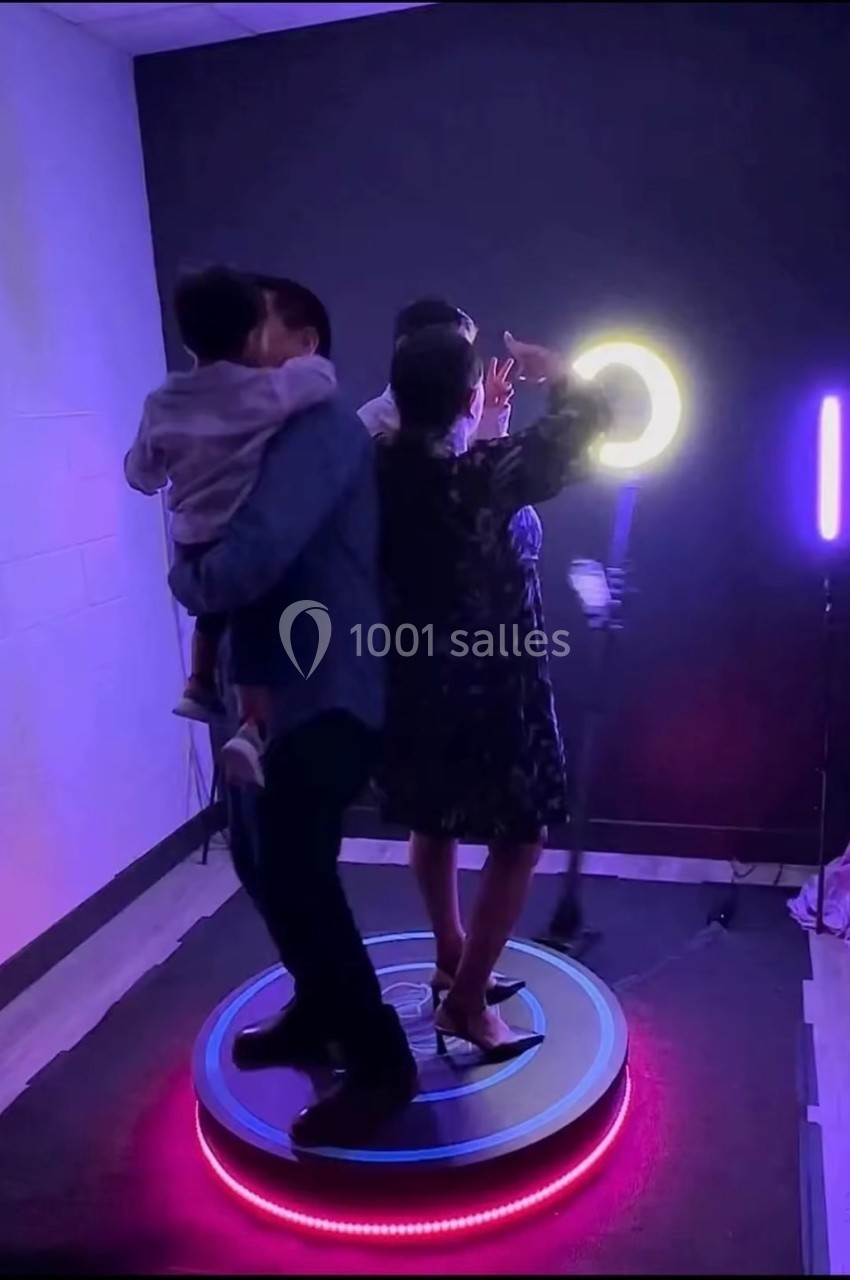 Des personnes debout sur une plateforme rotative, éclairées par des lumières colorées et un anneau lumineux.