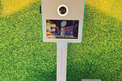 Borne photo avec éclairage, écran et accessoires humoristiques posés devant un mur végétal.