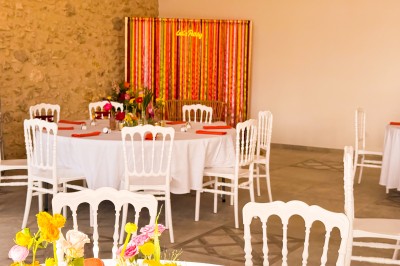 Centre de table floral coloré avec des roses et des verres disposés sur une nappe blanche, bougie en arrière-plan.