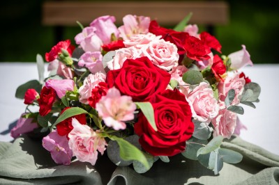 Centre de table floral coloré avec des roses et des verres disposés sur une nappe blanche, bougie en arrière-plan.