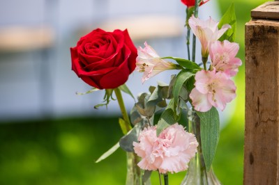 Centre de table floral coloré avec des roses et des verres disposés sur une nappe blanche, bougie en arrière-plan.