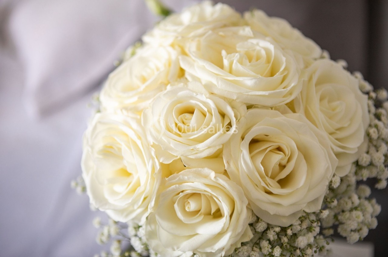 Bouquet de roses blanches entourées de petites fleurs blanches, posé sur un fond flou gris clair.