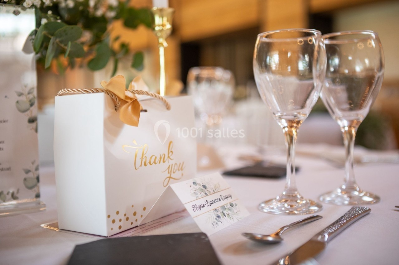 Boîte cadeau blanche avec inscription ’thank you’ sur une table dressée avec verres, couverts et décoration florale.