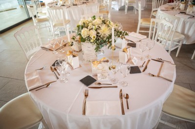 Centre de table floral coloré avec des roses et des verres disposés sur une nappe blanche, bougie en arrière-plan.