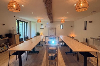 Salle spacieuse avec parquet clair, murs blancs, poutres apparentes et grandes baies vitrées donnant sur un jardin.