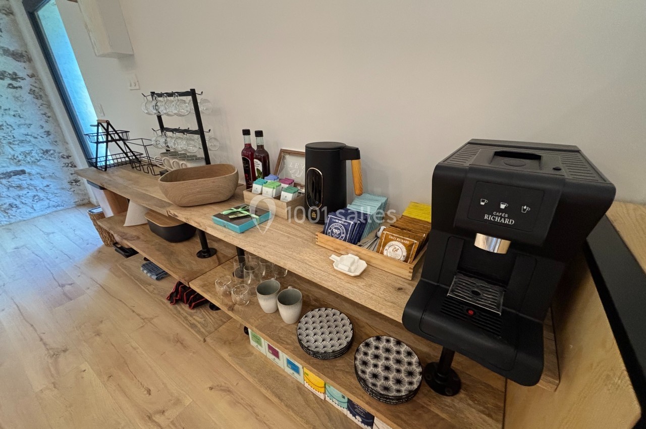 Espace de service avec machine à café, tasses, verres, thé, et accessoires disposés sur une étagère en bois.