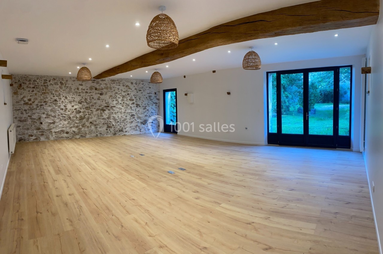 Salle lumineuse avec parquet en bois clair, murs en pierre et grandes baies vitrées donnant sur un espace vert.