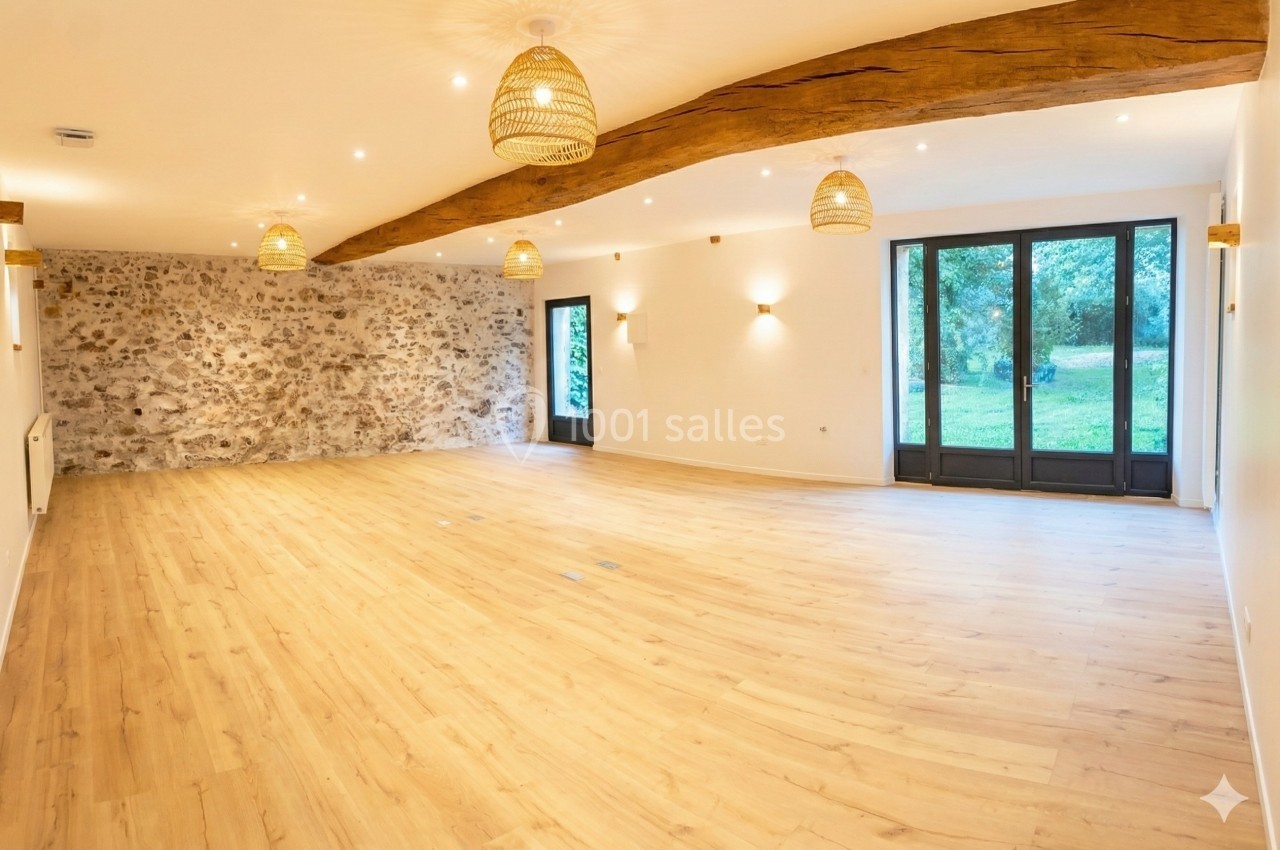 Salle lumineuse avec parquet en bois clair, mur en pierre apparente, poutre en bois et grandes baies vitrées donnant sur un…