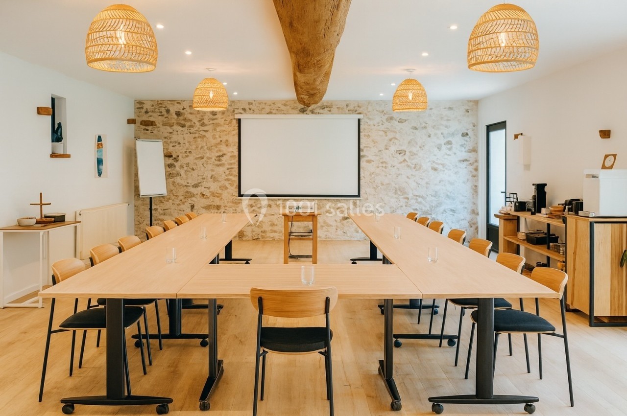 Salle de réunion lumineuse avec tables disposées en U, projecteur, écran blanc et décoration en bois et pierre.
