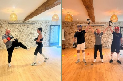 Deux personnes en équipement de boxe posent avec un entraîneur levant leurs bras dans une salle au sol en bois.