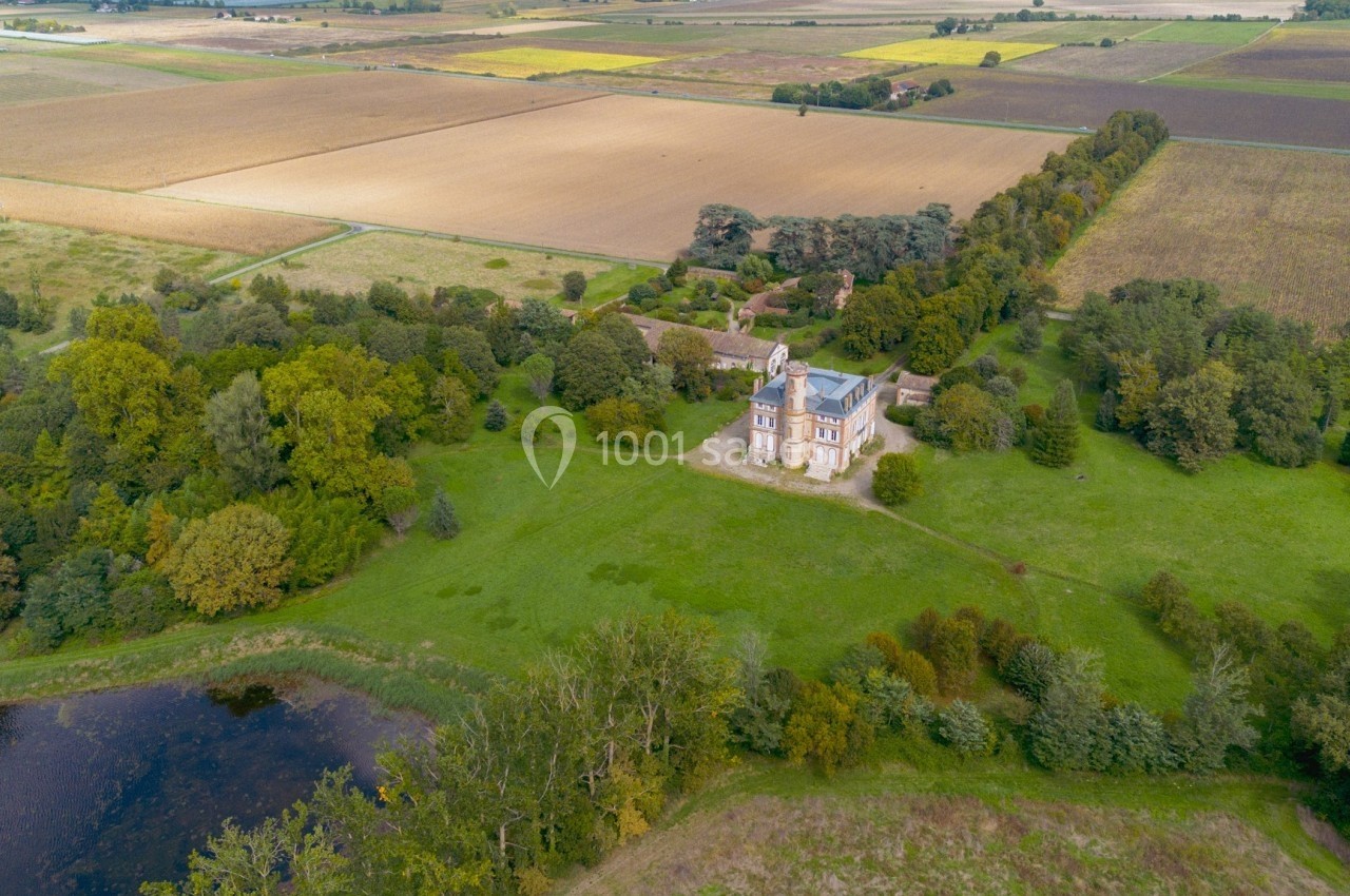Vue aérienne d'une église entourée d'arbres et de champs, avec un étang au premier plan.