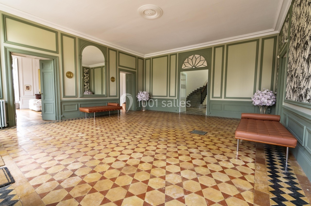Salle lumineuse avec sol en carreaux géométriques, murs vert clair ornés de moulures et bancs en cuir marron.