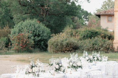 Un couple en tenue de mariage se tient devant une grande table décorée, avec un manoir en arrière-plan.