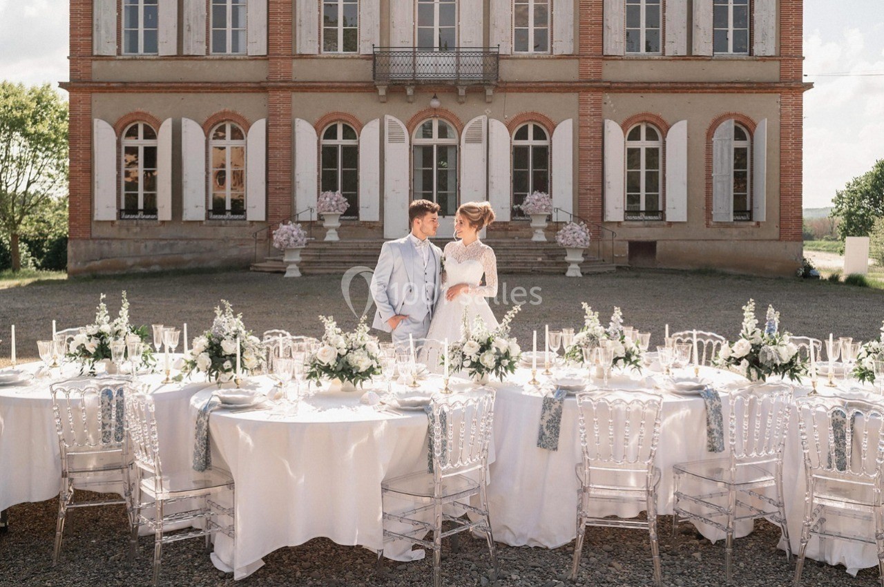 Un couple en tenue de mariage se tient devant une grande table décorée, avec un manoir en arrière-plan.