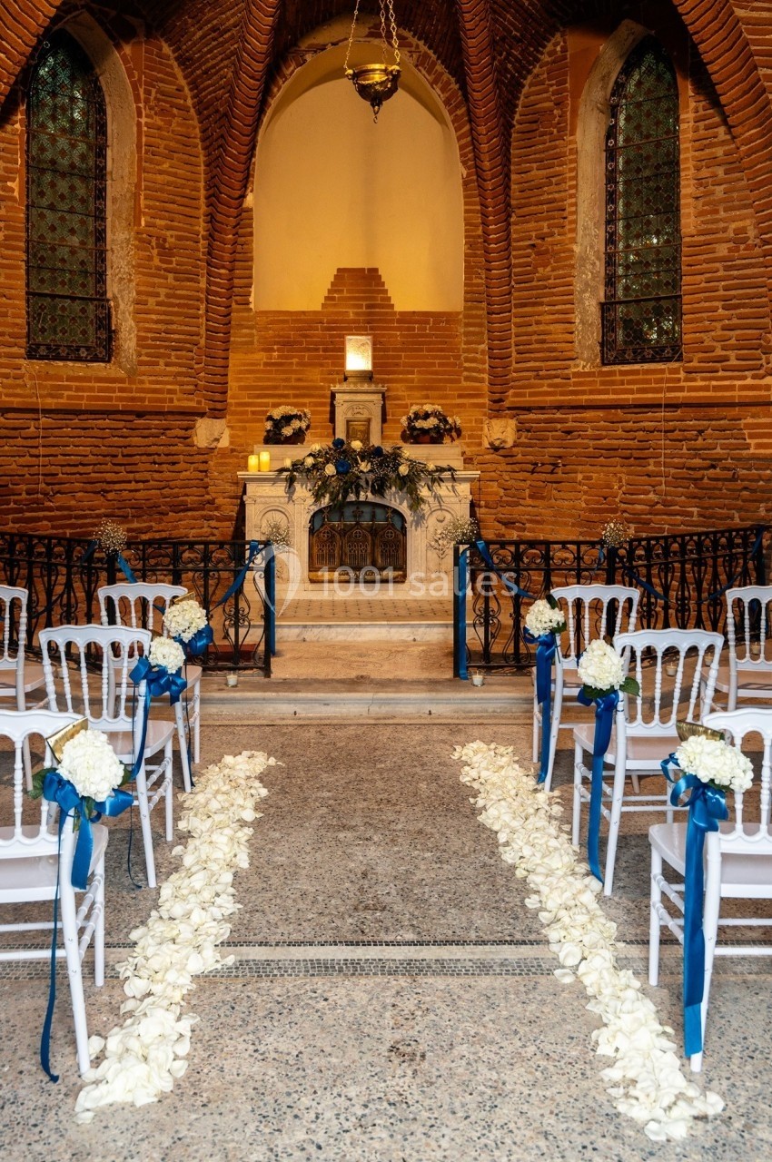 Allée décorée de pétales blancs menant à un autel dans une chapelle en briques avec des chaises ornées de fleurs.