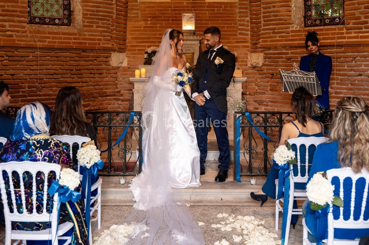 Un couple se tient devant un autel lors d'une cérémonie de mariage, entouré d'invités assis et de décorations florales.