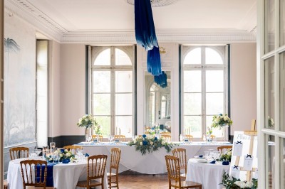 Tente blanche montée sur une pelouse, entourée de personnes et de tables, dans une cour avec bâtiments en arrière-plan.