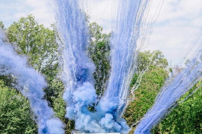 Tente blanche montée sur une pelouse, entourée de personnes et de tables, dans une cour avec bâtiments en arrière-plan.