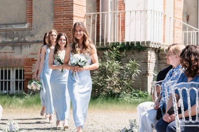 Tente blanche montée sur une pelouse, entourée de personnes et de tables, dans une cour avec bâtiments en arrière-plan.
