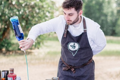 Tente blanche montée sur une pelouse, entourée de personnes et de tables, dans une cour avec bâtiments en arrière-plan.