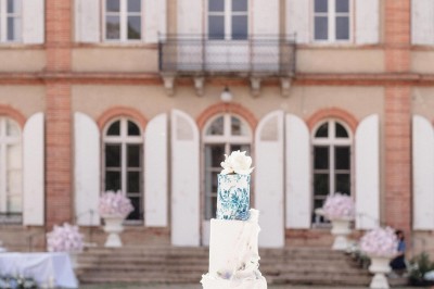 Tente blanche montée sur une pelouse, entourée de personnes et de tables, dans une cour avec bâtiments en arrière-plan.