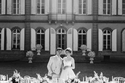 Tente blanche montée sur une pelouse, entourée de personnes et de tables, dans une cour avec bâtiments en arrière-plan.