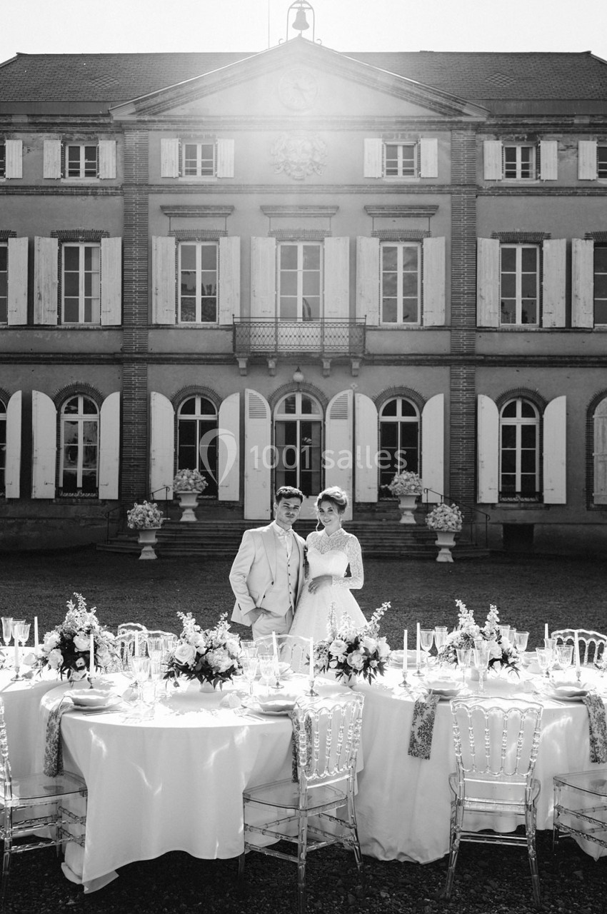 Un couple pose devant une table de réception décorée, avec un bâtiment historique en arrière-plan.