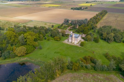 Tente blanche montée sur une pelouse, entourée de personnes et de tables, dans une cour avec bâtiments en arrière-plan.
