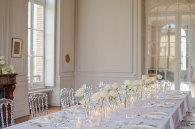 Tente blanche montée sur une pelouse, entourée de personnes et de tables, dans une cour avec bâtiments en arrière-plan.