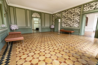 Tente blanche montée sur une pelouse, entourée de personnes et de tables, dans une cour avec bâtiments en arrière-plan.