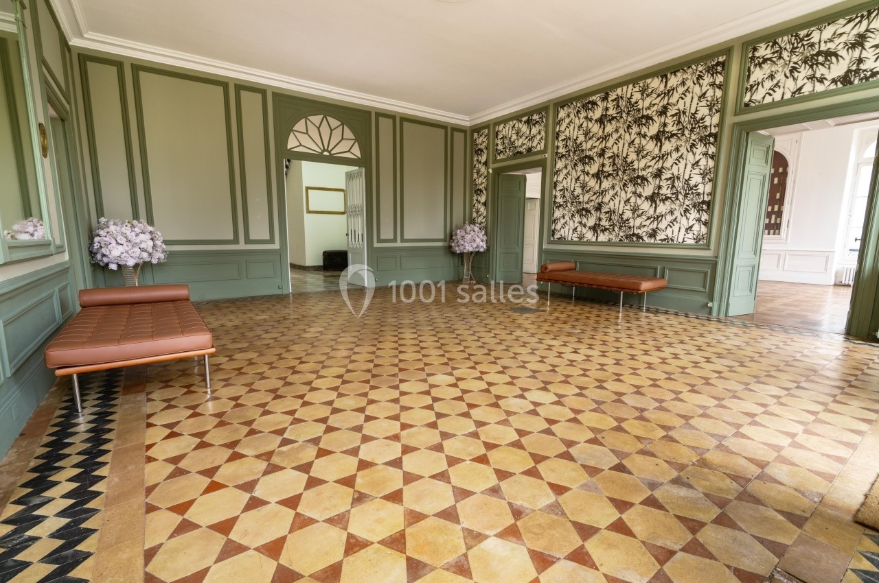 Salle lumineuse avec carrelage géométrique, murs verts, bancs en cuir et décoration florale dans un intérieur classique.