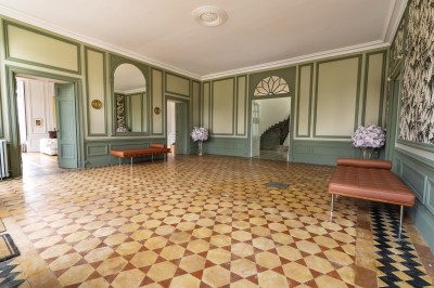 Tente blanche montée sur une pelouse, entourée de personnes et de tables, dans une cour avec bâtiments en arrière-plan.