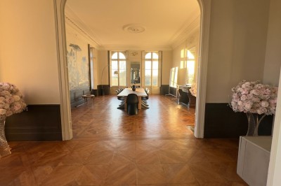 Tente blanche montée sur une pelouse, entourée de personnes et de tables, dans une cour avec bâtiments en arrière-plan.