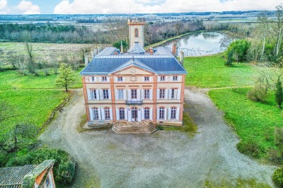 Tente blanche montée sur une pelouse, entourée de personnes et de tables, dans une cour avec bâtiments en arrière-plan.