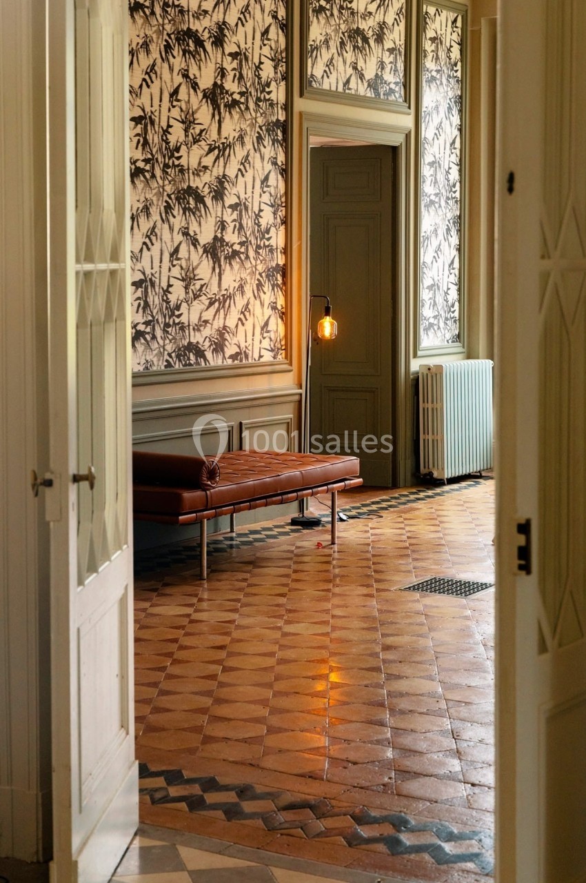 Vue d'un intérieur élégant avec un banc en cuir, un sol en carreaux anciens et une lampe allumée près d'une porte.